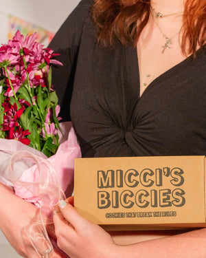 Person holding a box labeled 'Micci's Biccies' with flowers on the side.